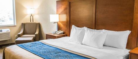 Ein Hotelzimmer mit einem großen Bett, einem Holzkopfende, einem Schreibtisch mit Lampe, einem Stuhl und einem Fenster mit Tageslicht.