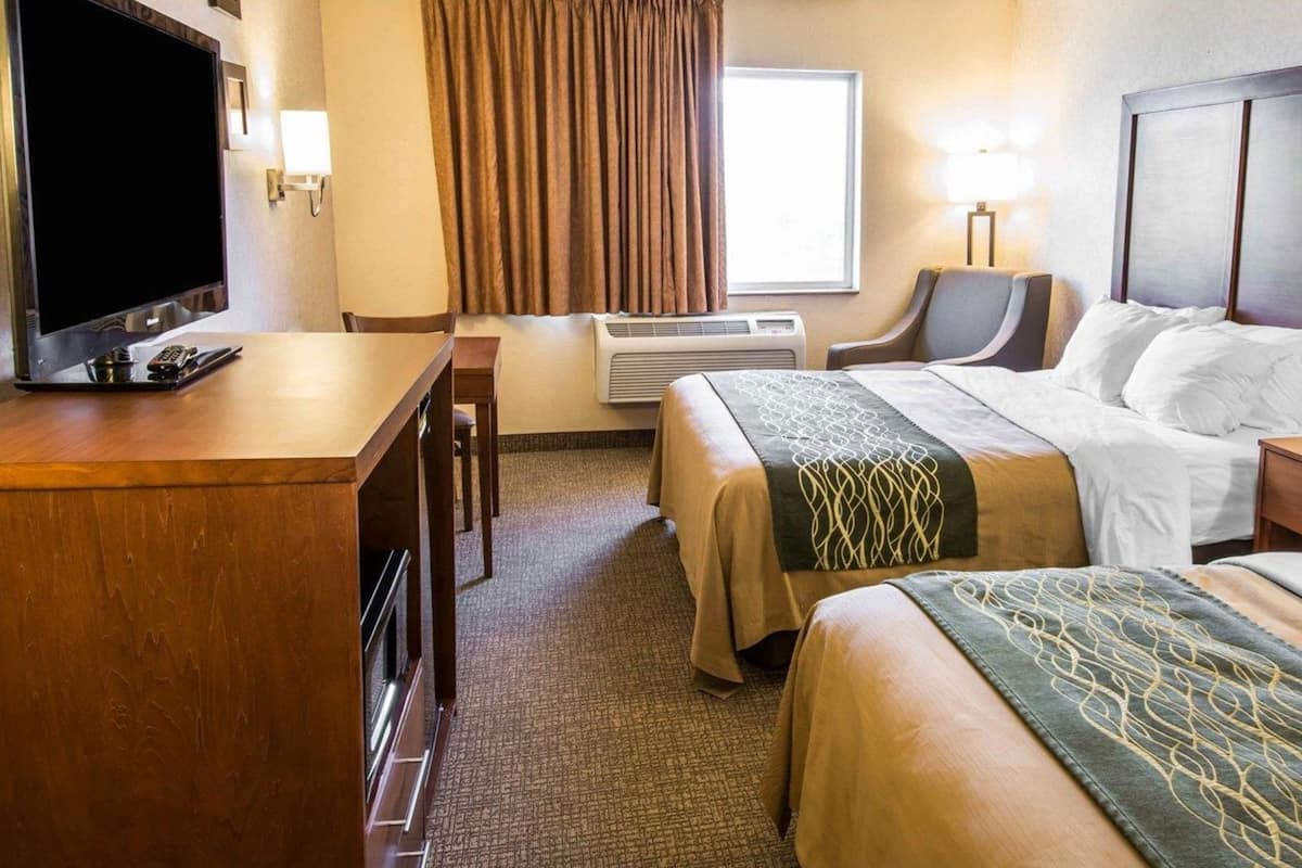 A hotel room with a bed, a desk, a TV, a chair, a window with curtains, and a lamp.