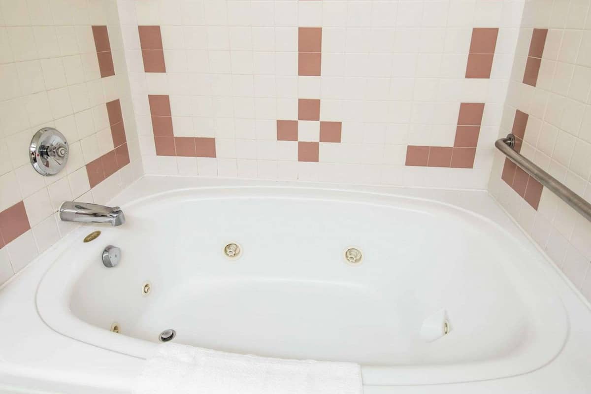 A white bathtub with a chrome faucet and control knobs, set against a wall with a checkered tile pattern.