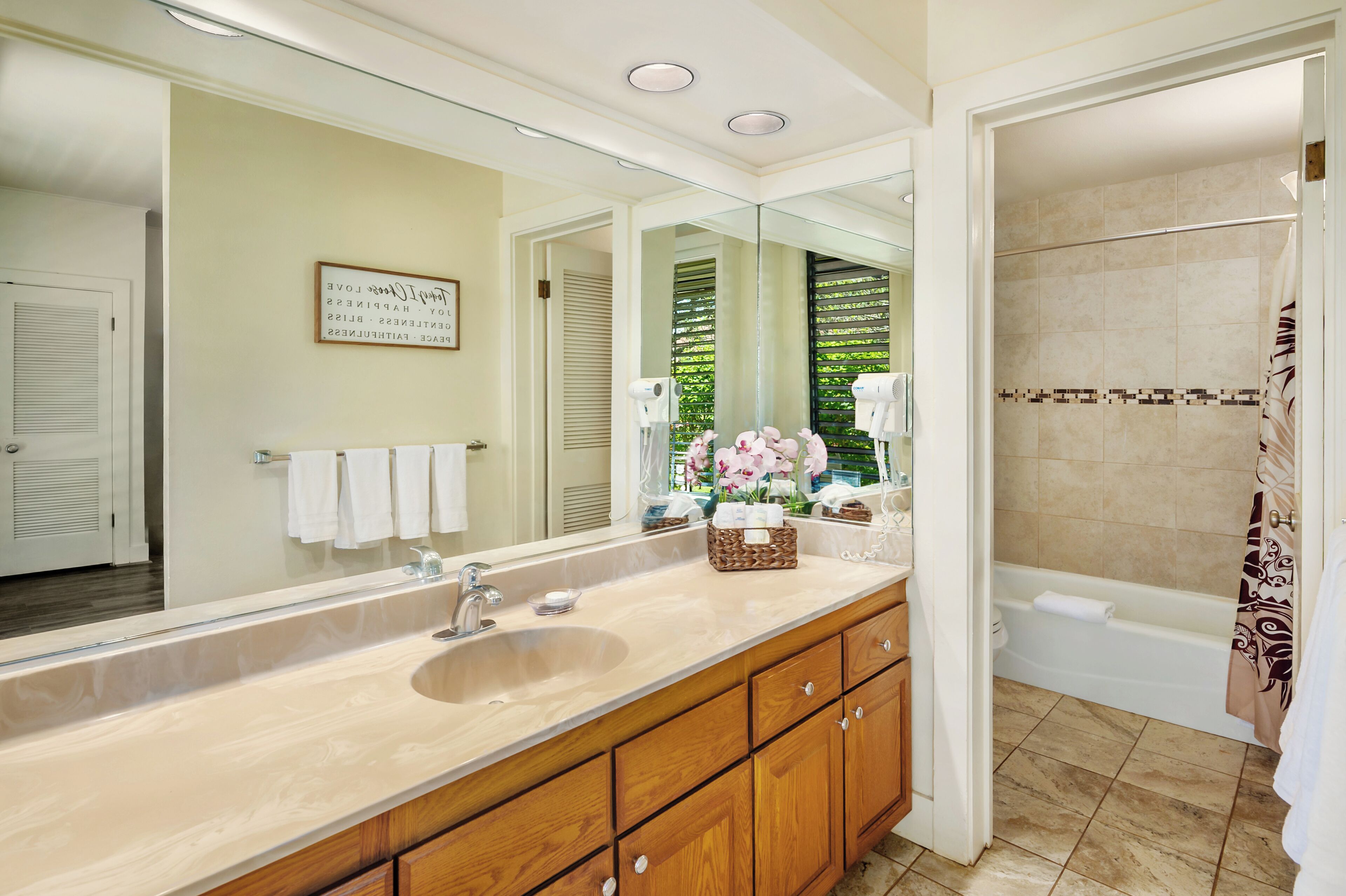 A bathroom with a large mirror, a sink, wooden cabinets, a shower area, and a towel rack.