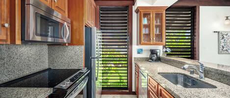 A kitchen with wooden cabinets, a stainless steel microwave, a refrigerator, a stove, a sink, and a window with blinds.