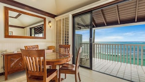 Un coin repas avec une table ronde et des chaises en bois, un grand miroir et une porte-fenêtre coulissante donnant sur un balcon avec vue sur l’océan.