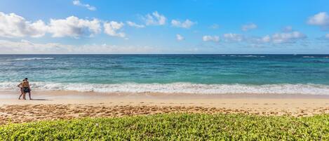 A beach with a person standing on the sand, a clear sky, and the ocean.