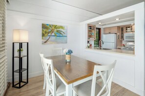 Una cocina moderna con armarios blancos, una mesa de comedor de madera y un cuadro con una playa.