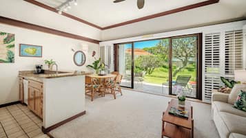Amplia sala de estar con cocina, mesa de comedor y puerta corredera de vidrio que da a un jardín.