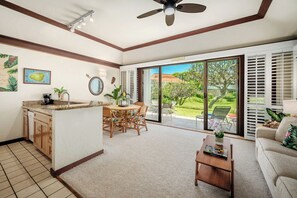 Amplia sala de estar con cocina, mesa de comedor y puerta corredera de vidrio que da a un jardín.