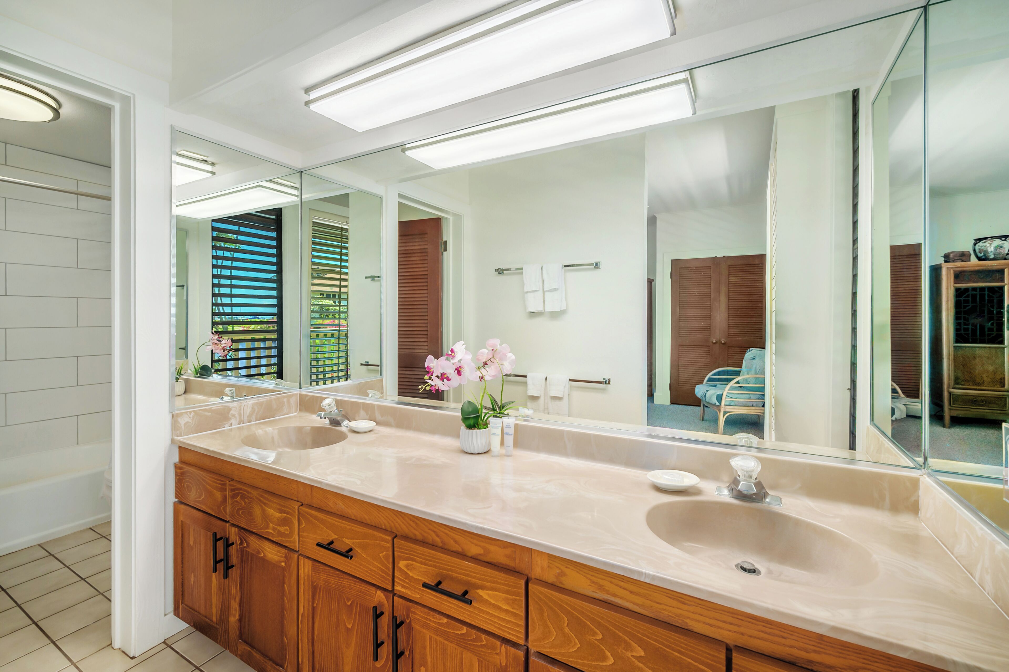 A modern bathroom with a large mirror, two sinks, wooden cabinetry, and a potted orchid.