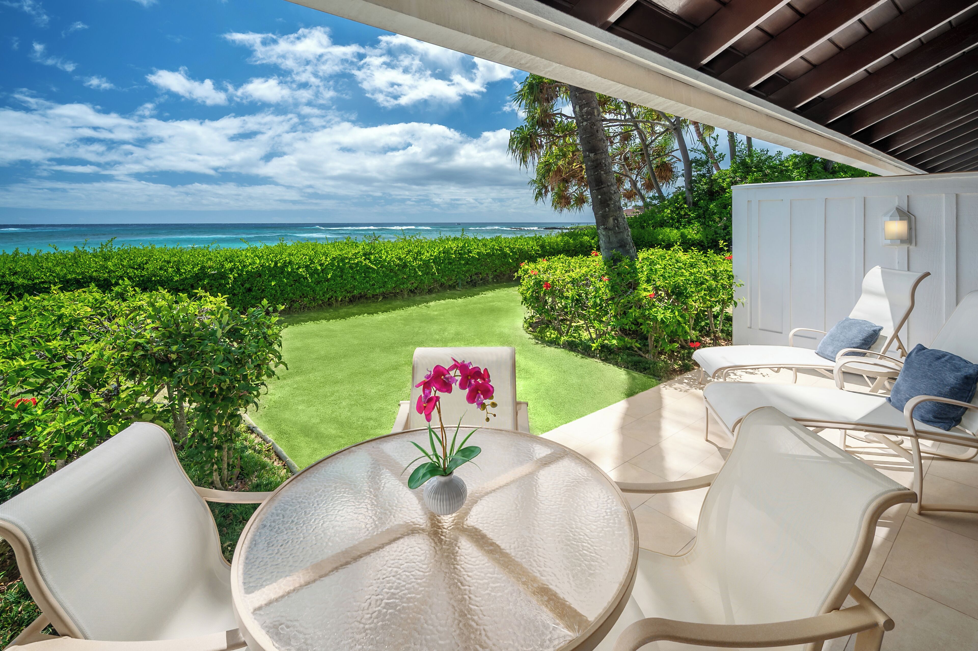 Une terrasse avec une table en verre, des chaises blanches et une vue sur l’océan.