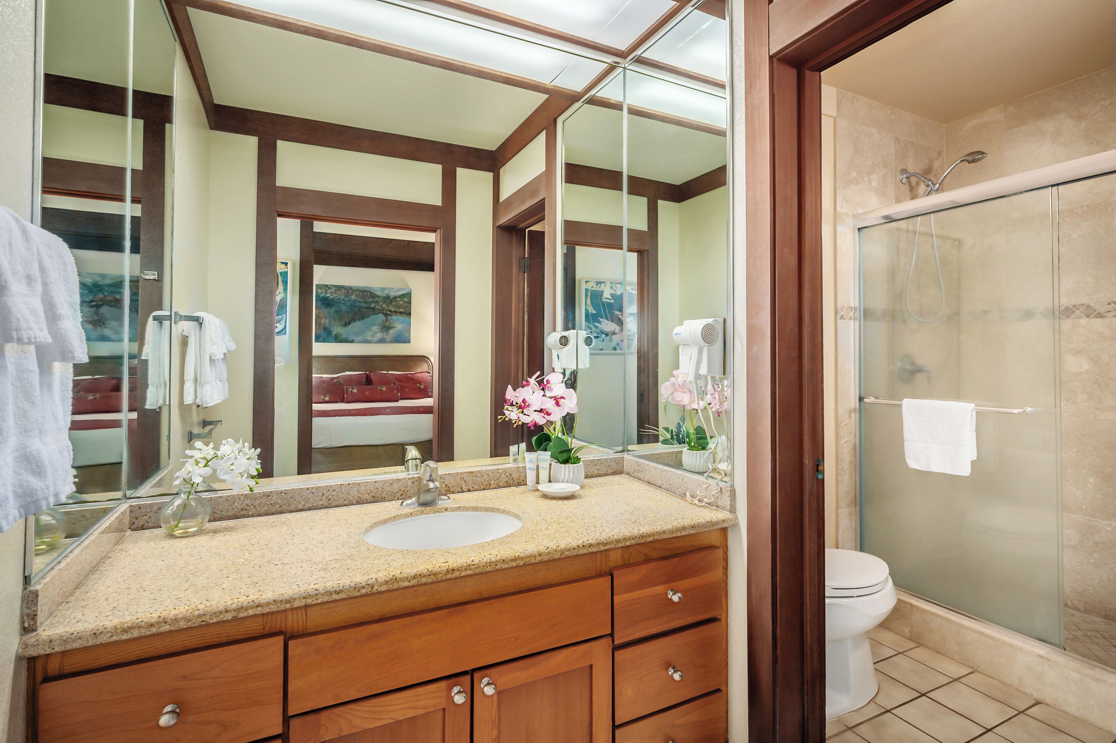 Un baño con tocador de madera, un espejo grande, cabina de ducha de vidrio y un inodoro.