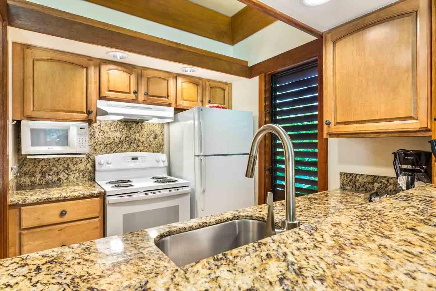 A kitchen with granite countertops, a stove, a microwave, a refrigerator, and wooden cabinets.