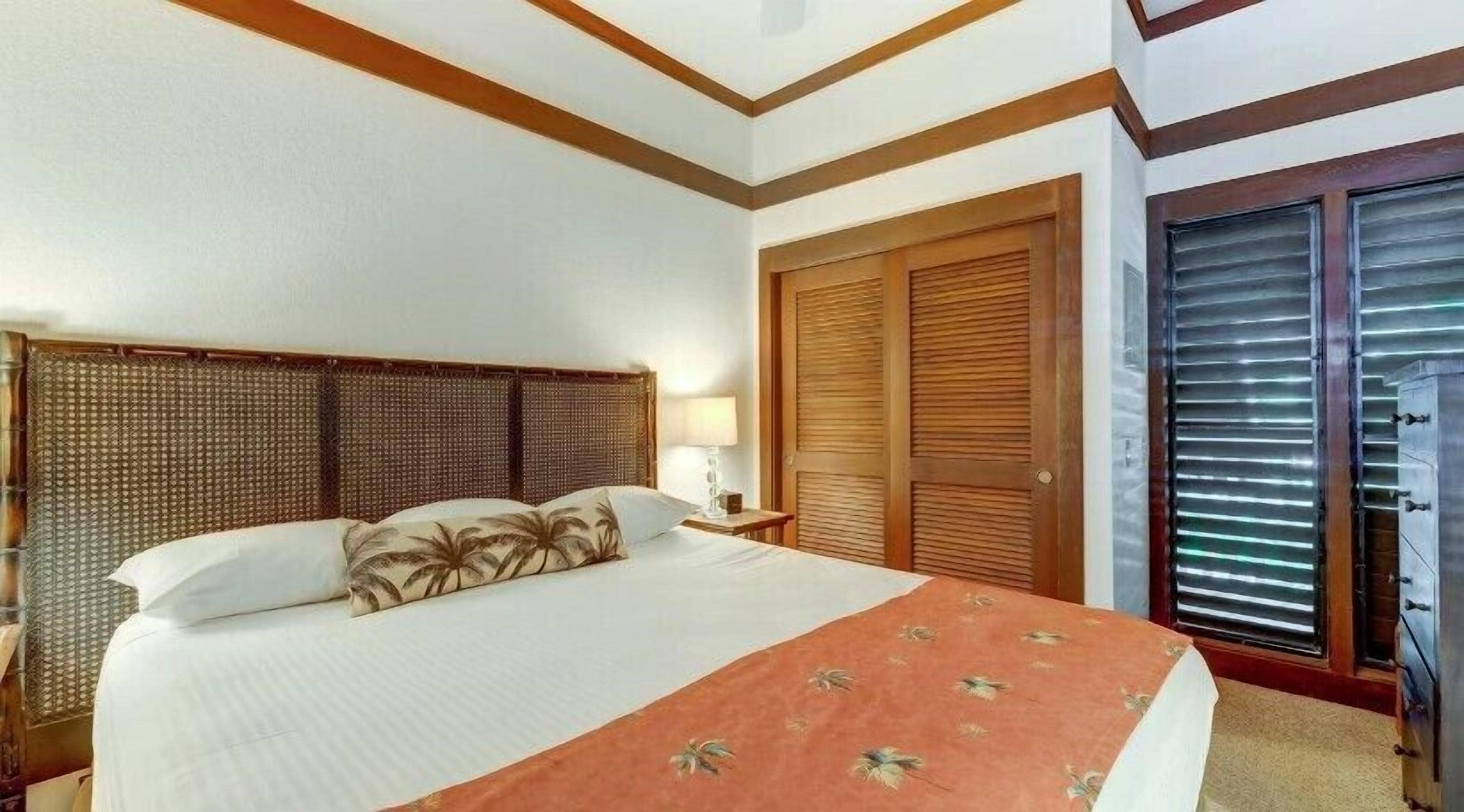 A hotel room with a large bed, a wooden headboard, a nightstand with a lamp, and a sliding glass door leading to a balcony.