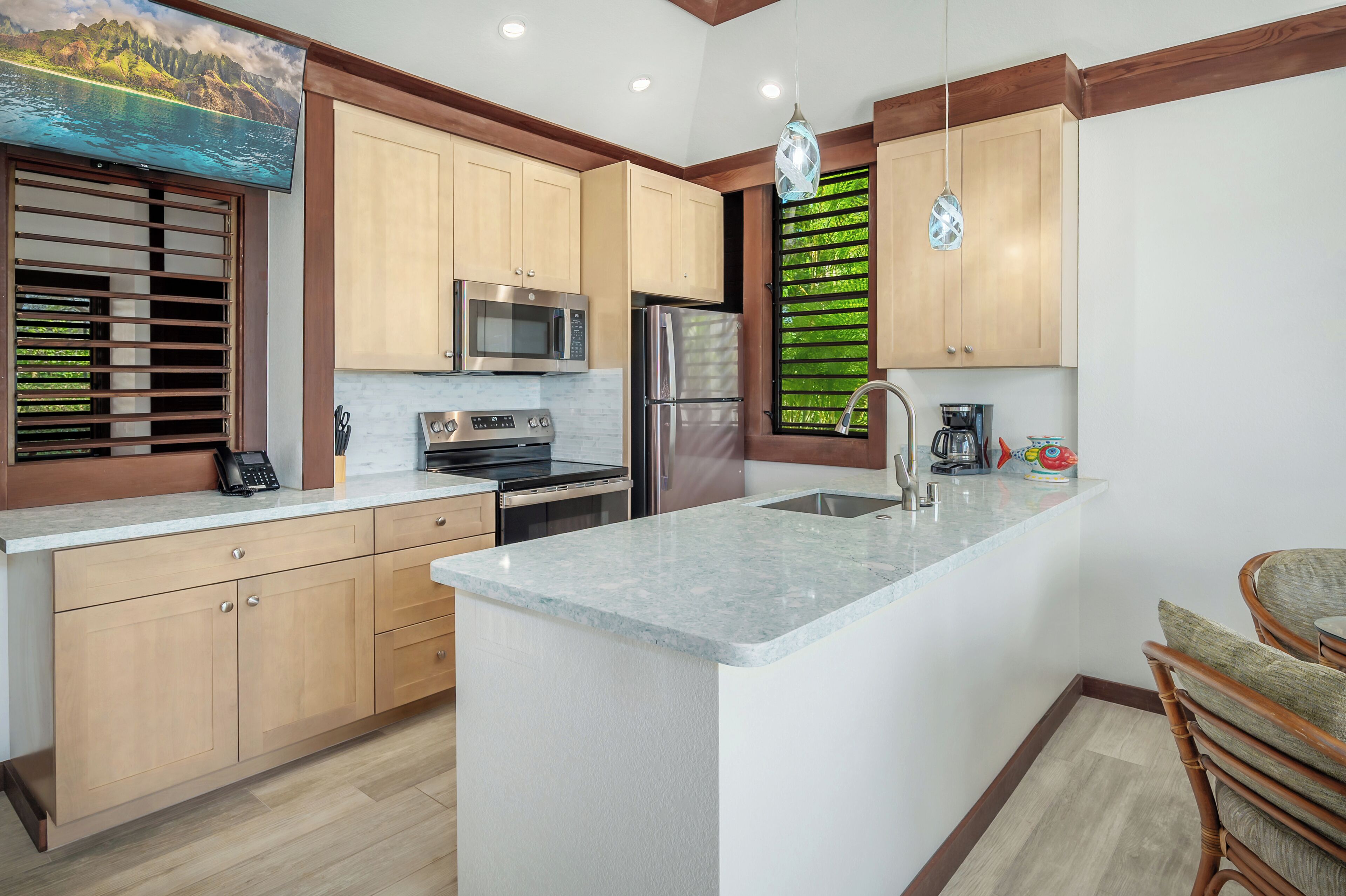 A modern kitchen with wooden cabinets, a stainless steel refrigerator, a microwave, and a large island with a sink.