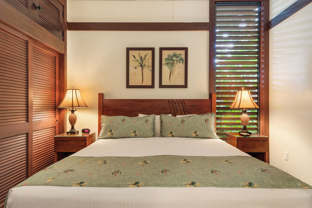 Une chambre d’hôtel avec un grand lit, deux tables de chevet, une tête de lit en bois et une fenêtre avec des stores.