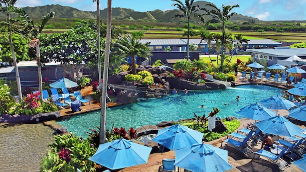 Un espace piscine agrémenté de chaises longues et de parasols, entouré de plantes tropicales et offrant une vue sur les montagnes lointaines.