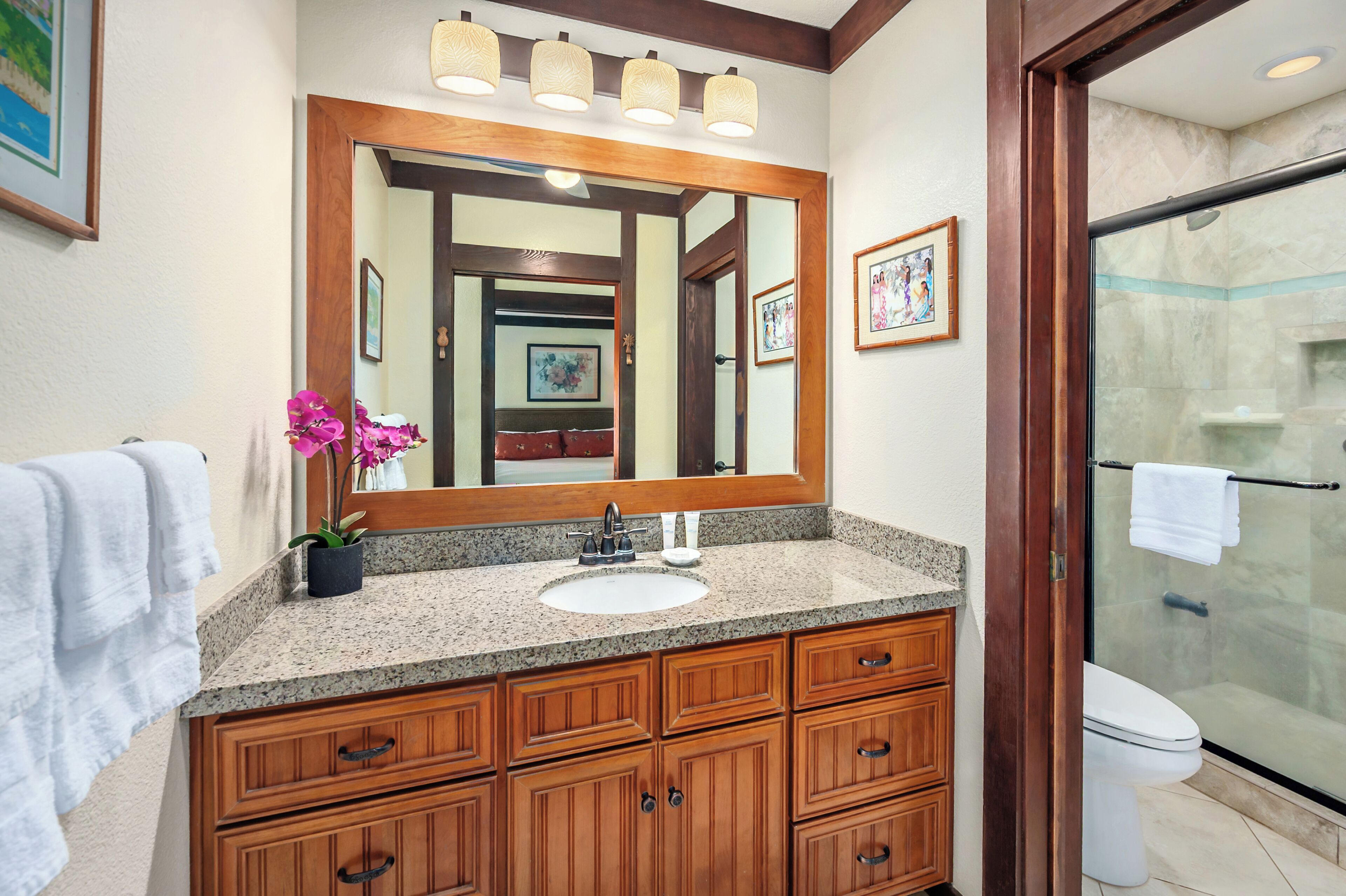 A bathroom with a granite countertop sink, wooden vanity, a large mirror, and a glass shower enclosure.