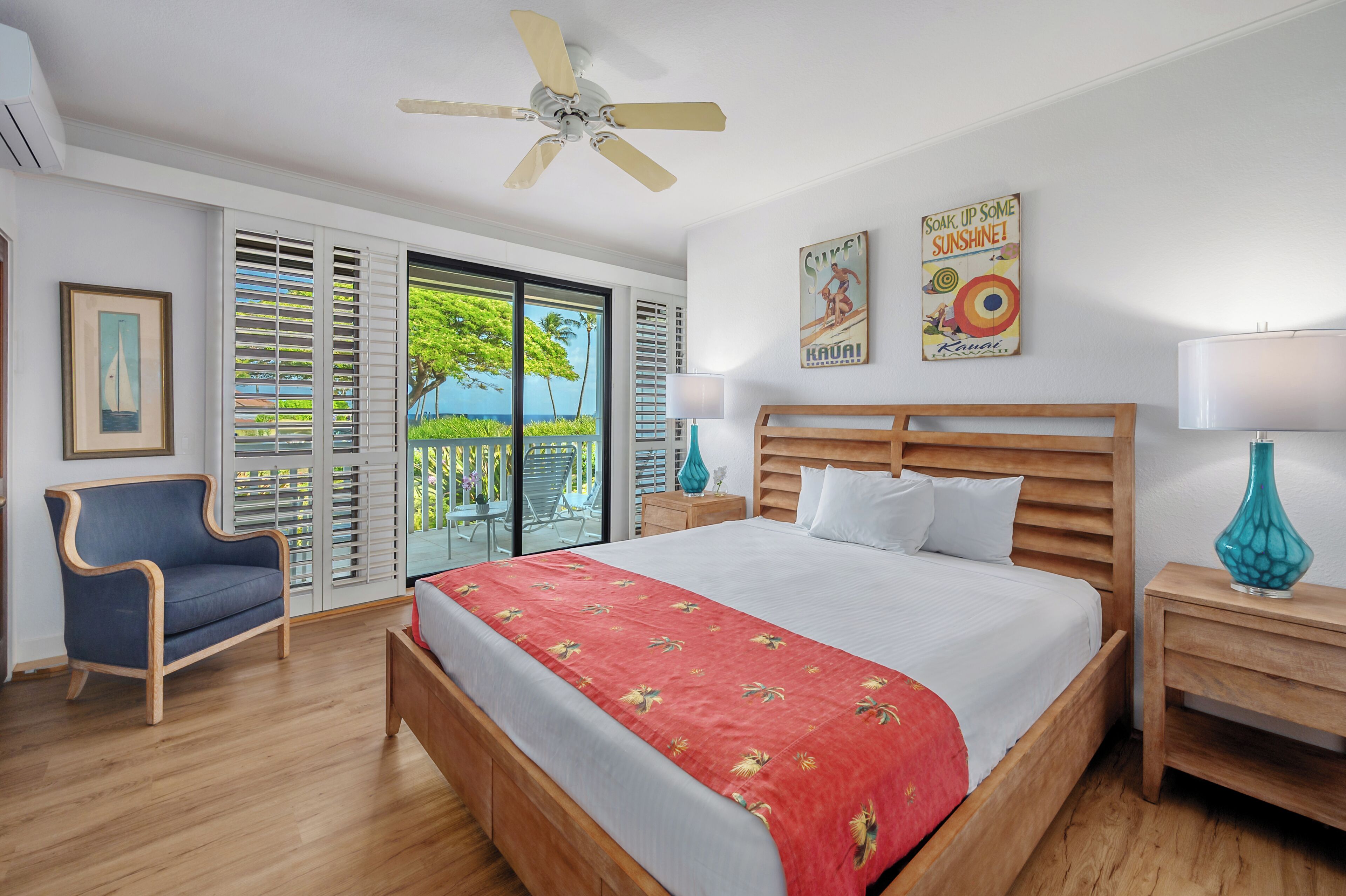 A hotel room with a large bed, wooden headboard, two nightstands, a ceiling fan, a window with shutters, and a view of the outdoors.
