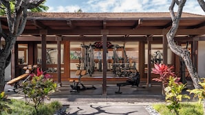 A covered outdoor gym area with exercise equipment, a wooden deck, and surrounding greenery.
