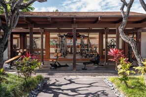 A covered outdoor gym area with exercise equipment, a wooden deck, and surrounding greenery.