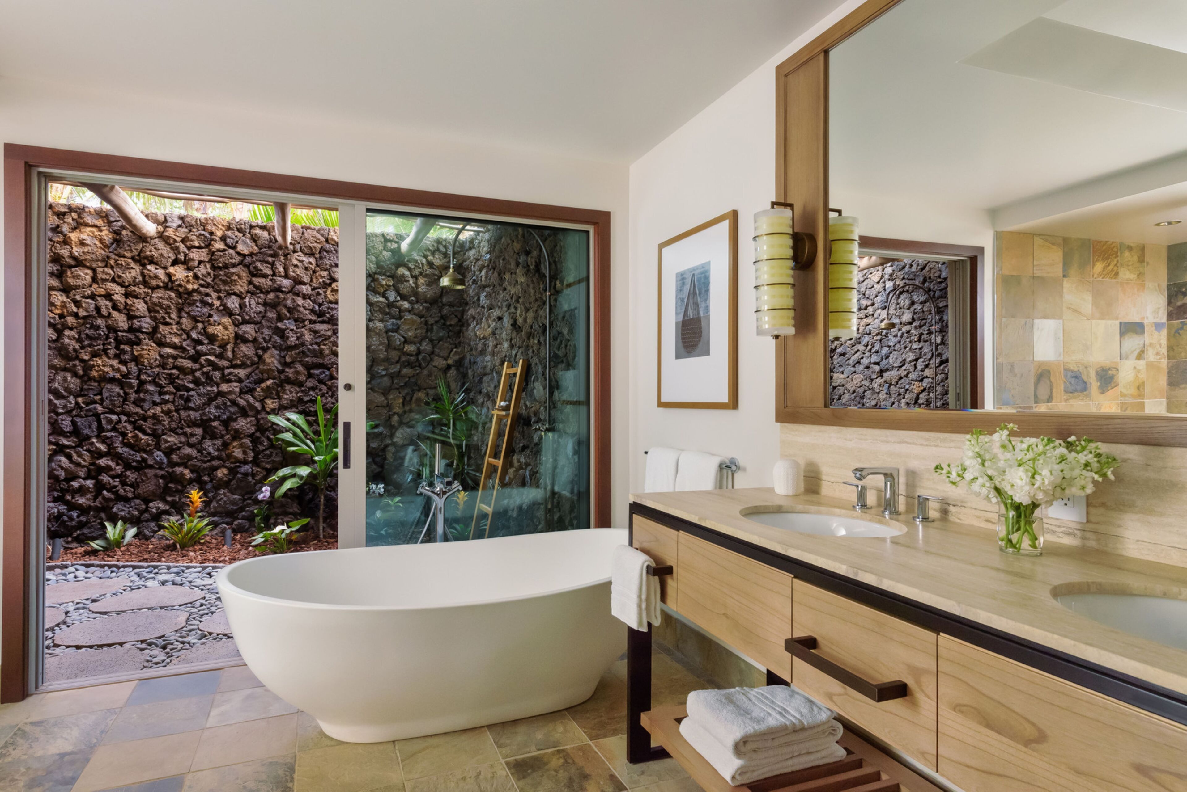 Un baño moderno con una bañera independiente, un espejo grande y un fondo de pared de piedra.