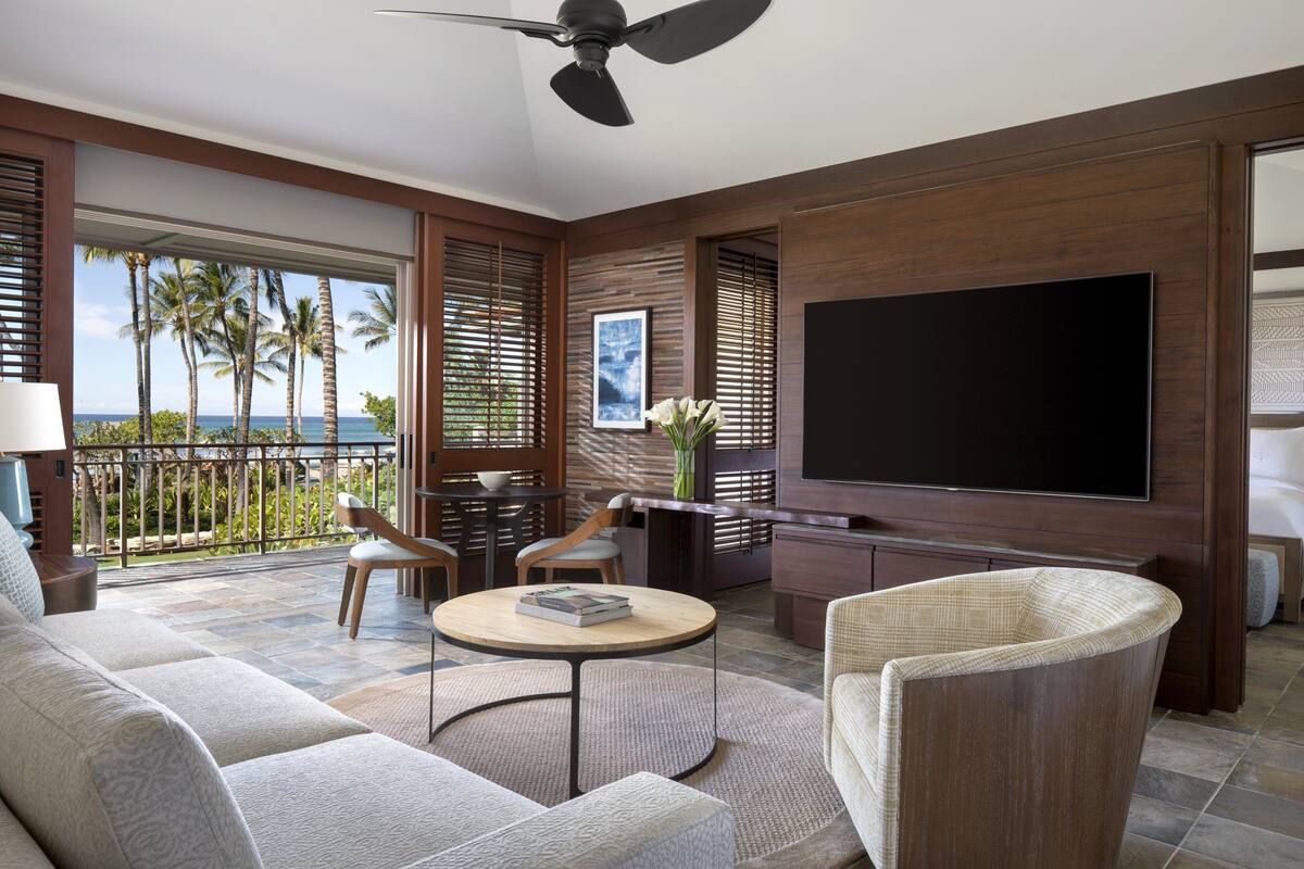 Una sala de estar moderna con un televisor de pantalla plana grande, asientos cómodos y vistas a palmeras.