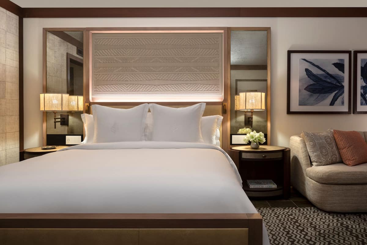 Un cuarto de hotel con una cama grande, dos mesitas de noche, una silla y cuadros en la pared.