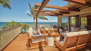 Une terrasse en bois avec des sièges, une plante en pot et une vue sur l’océan.