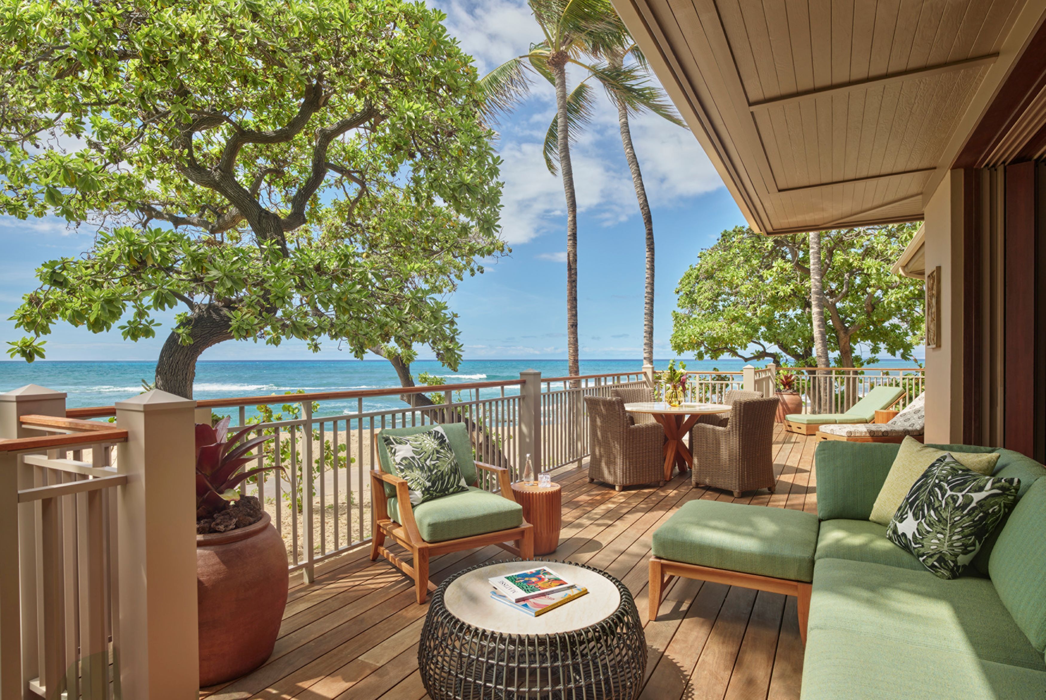 A wooden deck with outdoor furniture, a large tree, and a view of the ocean.