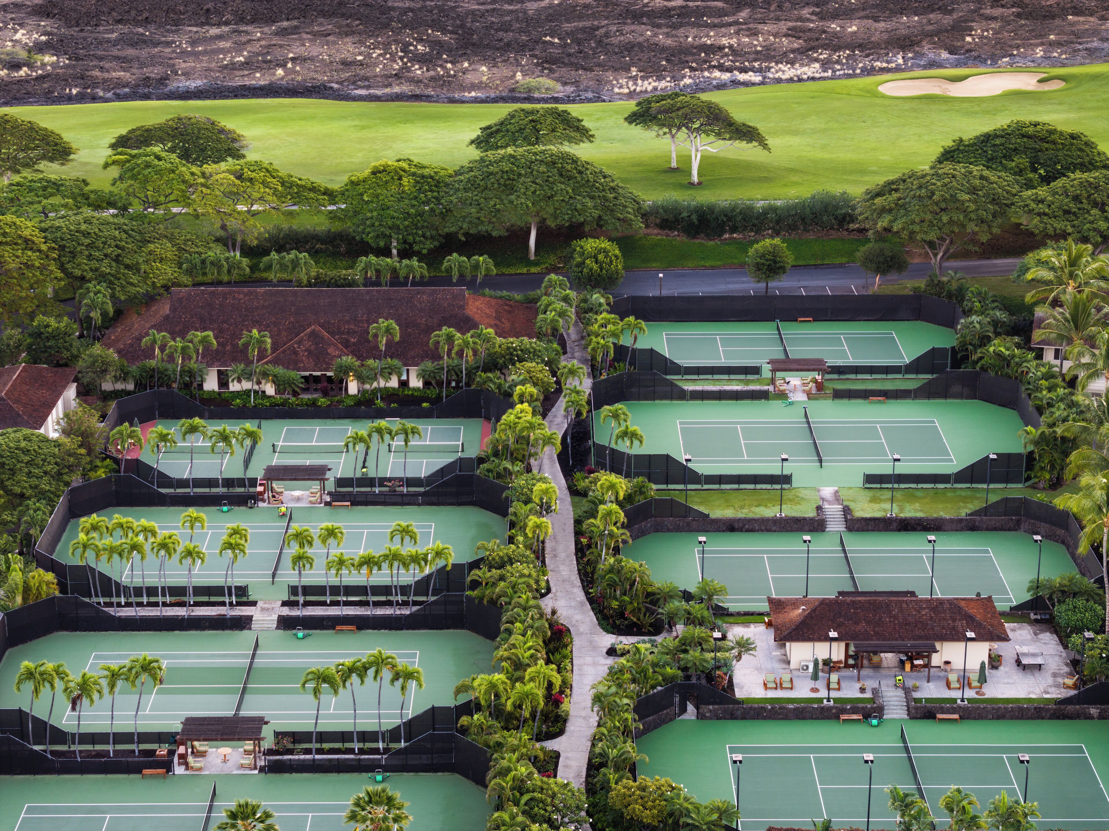 Tenniscomplex met meerdere velden, palmbomen en een golfbaan op de achtergrond.