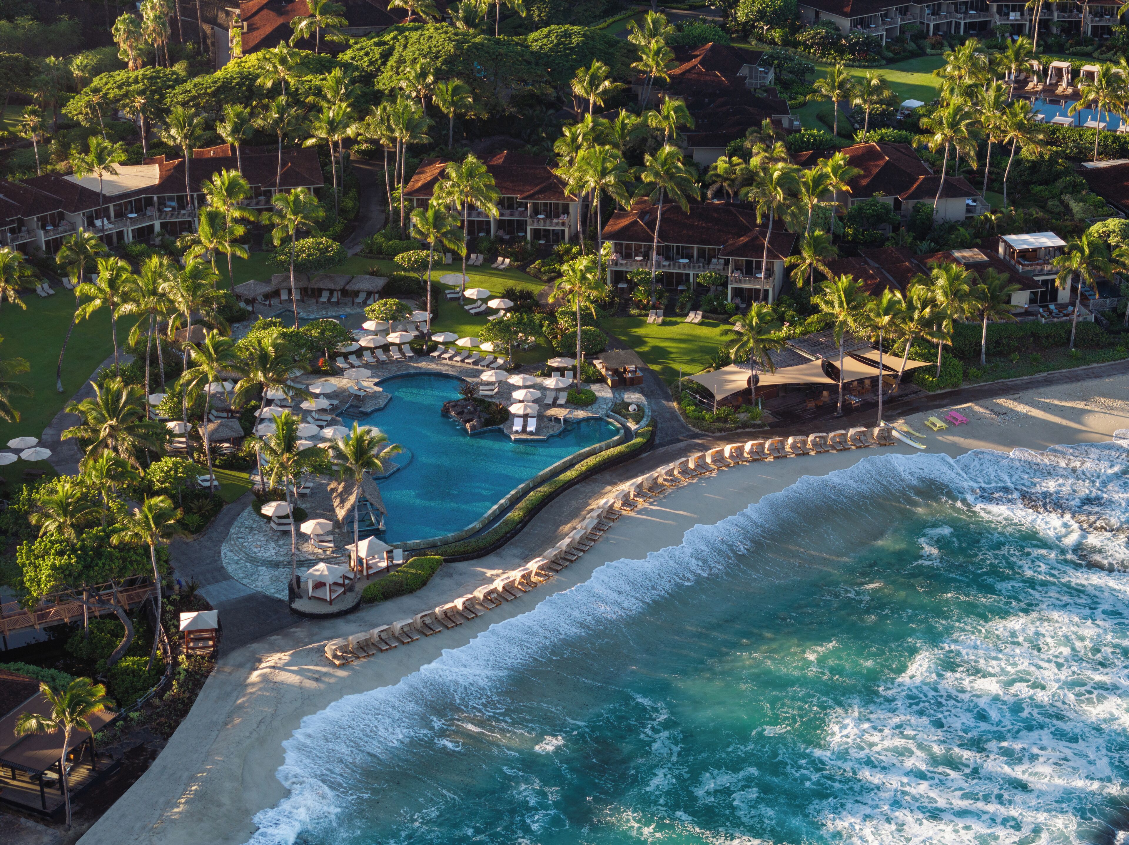 Oversigtsbillede af et resort med central swimmingpool, strandpromenade og frodig beplantning.