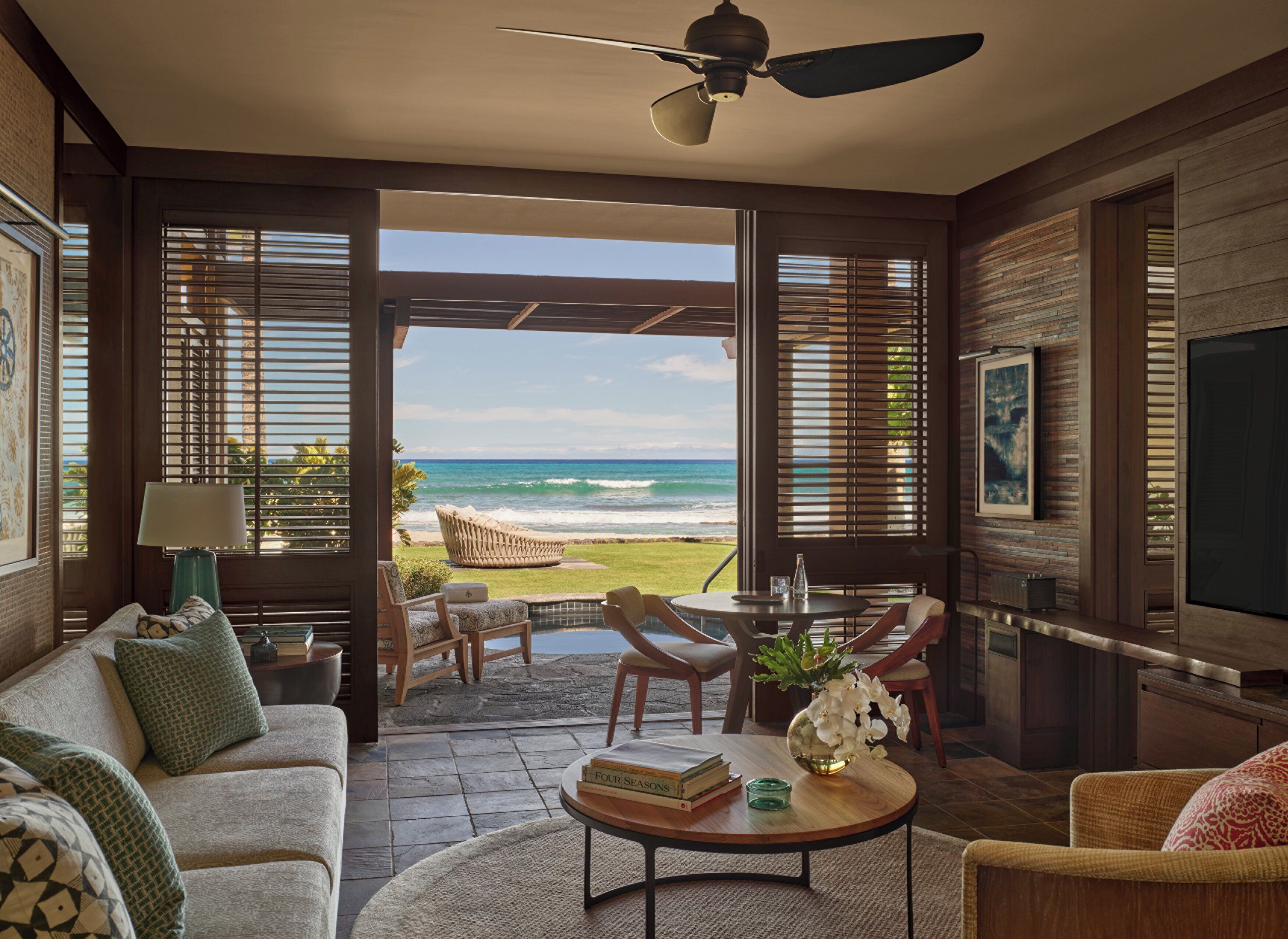 A room with a view of the ocean, a ceiling fan, a sofa, a coffee table, and a dining area with chairs.