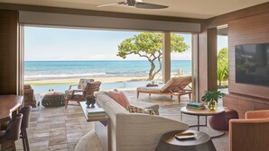 Il s’agit d’une pièce spacieuse dotée d’une grande fenêtre donnant sur une plage et l’océan. On y trouve un coin salon avec un canapé, des fauteuils et une petite table. Un téléviseur est fixé au mur.
