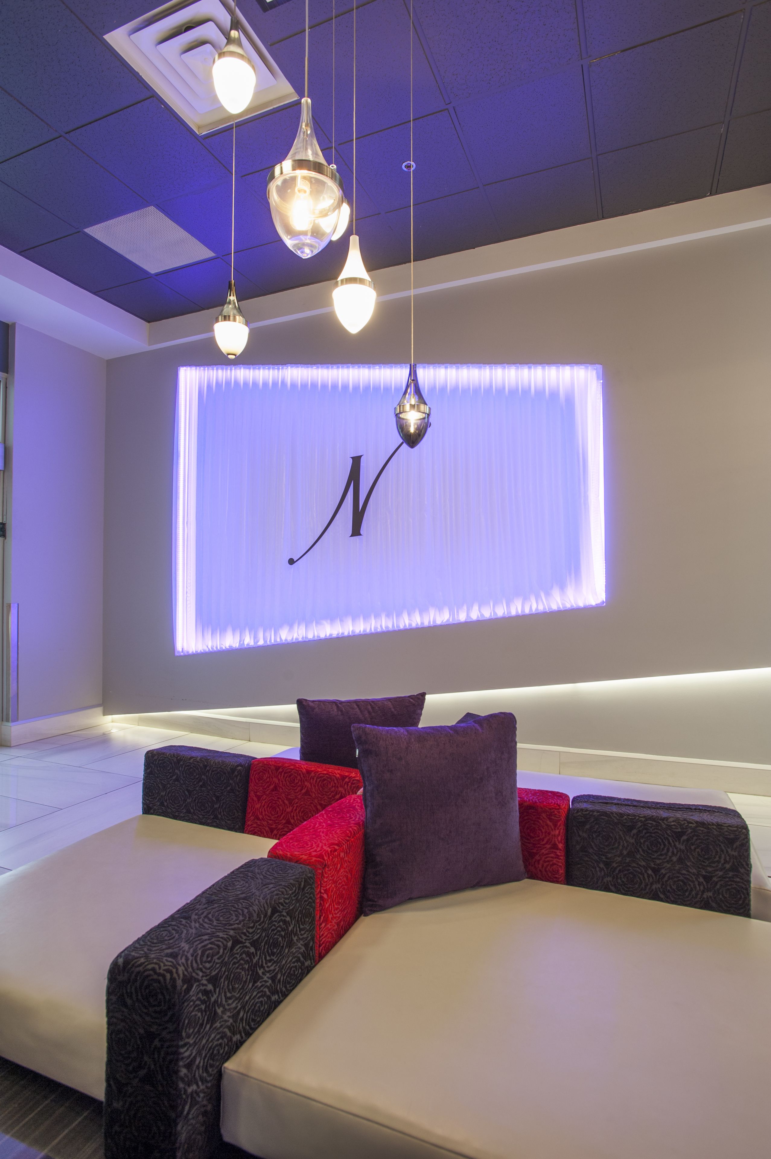 A modern lounge area with a sofa set, pendant lighting, and a large illuminated wall with a letter.