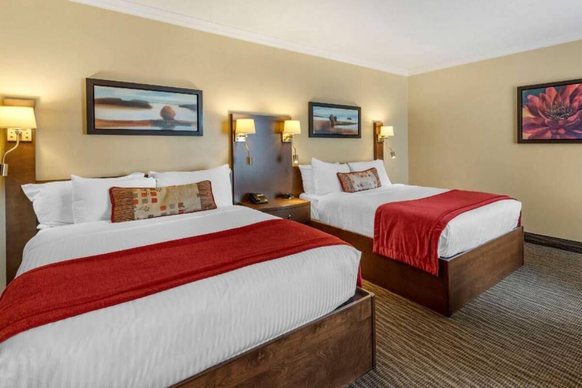 A hotel room with two beds, each with a red blanket, a nightstand with a lamp, and wall-mounted artwork.