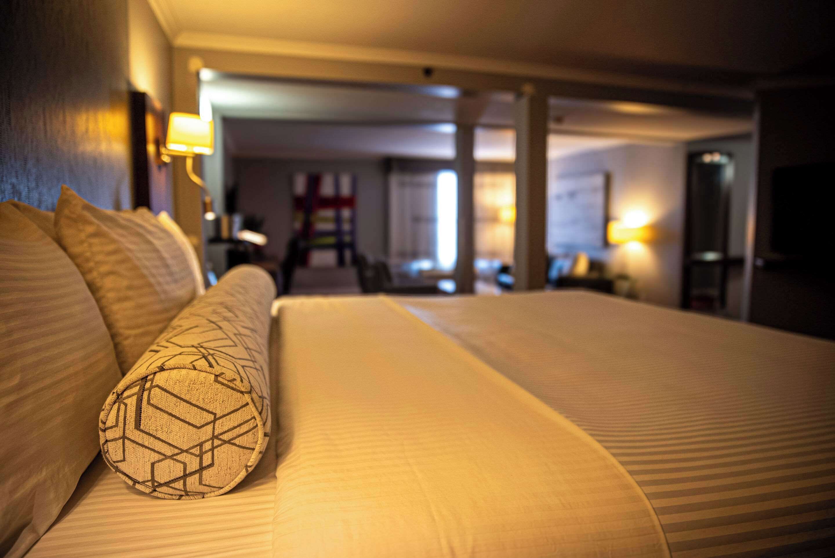 Quarto de hotel com uma cama grande, cabeceira e uma luminária na parede.