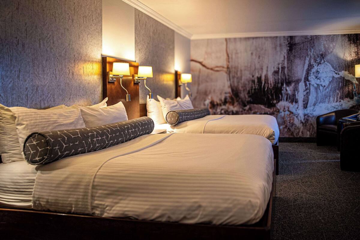 A hotel room with two beds, each with a patterned pillow, a headboard, and wall-mounted lamps.