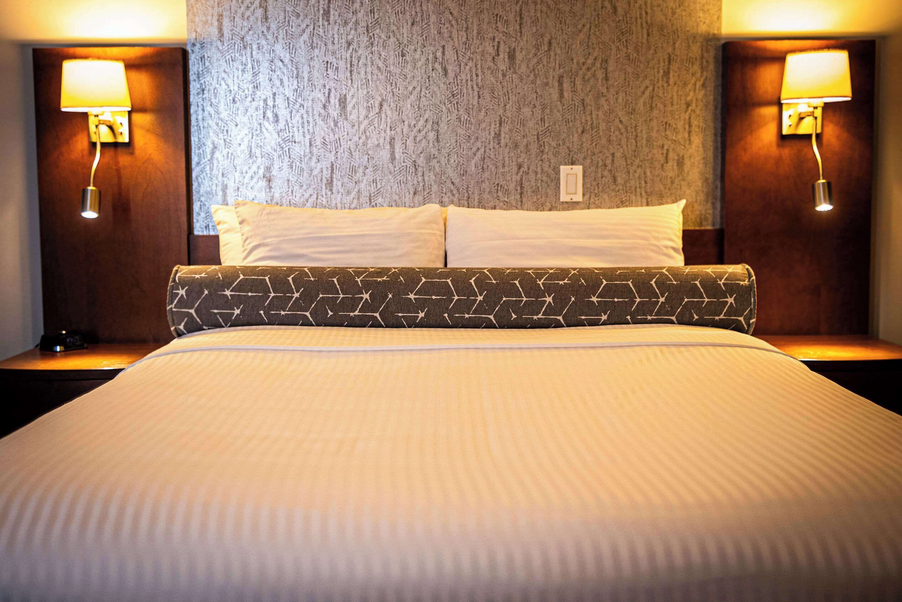 A hotel room with a large bed, two bedside lamps, and a textured wall behind the bed.