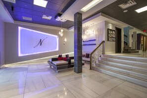 A modern lobby with a large illuminated 'N' on the wall, a sofa with red cushions, and a staircase. - Le Noranda Hotel & Spa, an Ascend Collection Hotel (Rouyn-Noranda)
