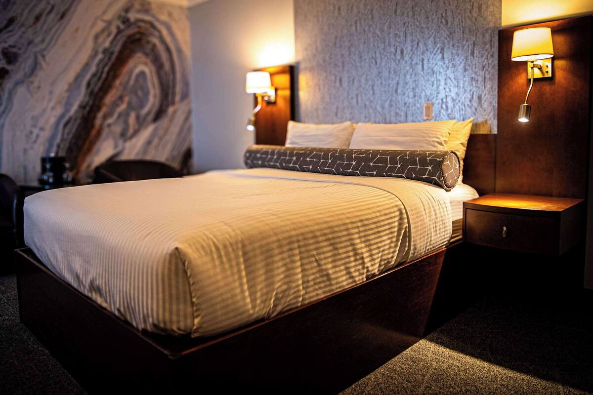 A neatly made bed with a striped bedspread, two bedside lamps, and a marble wall behind.