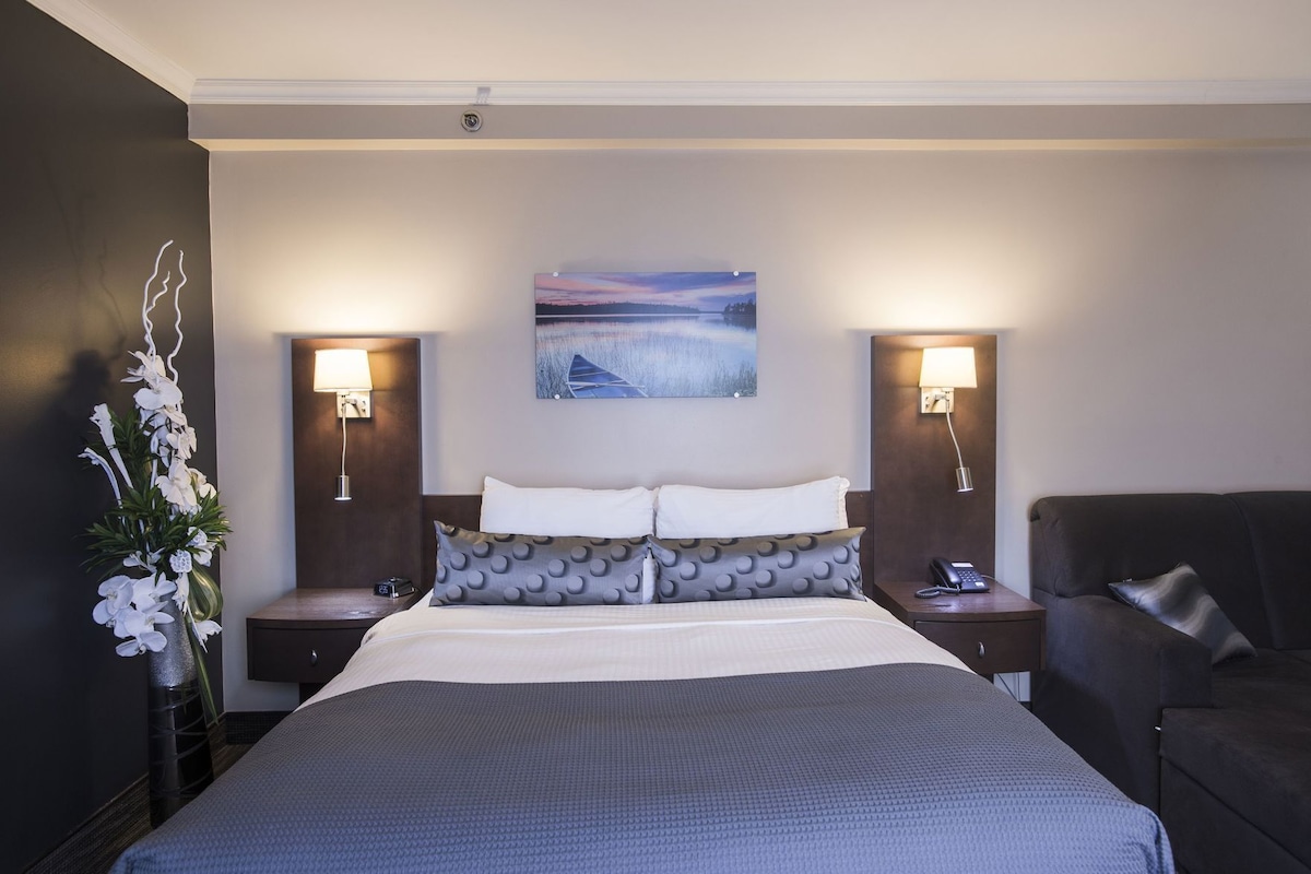 A hotel room with a large bed, two bedside lamps, a nightstand, a couch, and a wall-mounted painting.