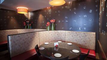 Un restaurante con una mesa redonda preparada para cuatro comensales, asientos tapizados en rojo y papel tapiz con estampado floral.