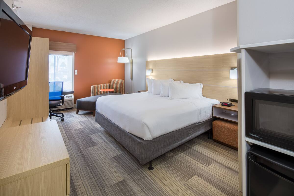 A hotel room with a bed, a desk, a chair, a TV, and a microwave.