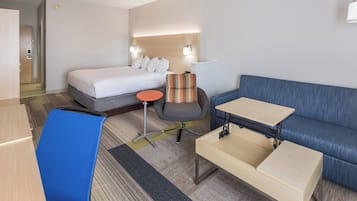 A hotel room with a bed, a desk, a chair, a sofa, and a small table.