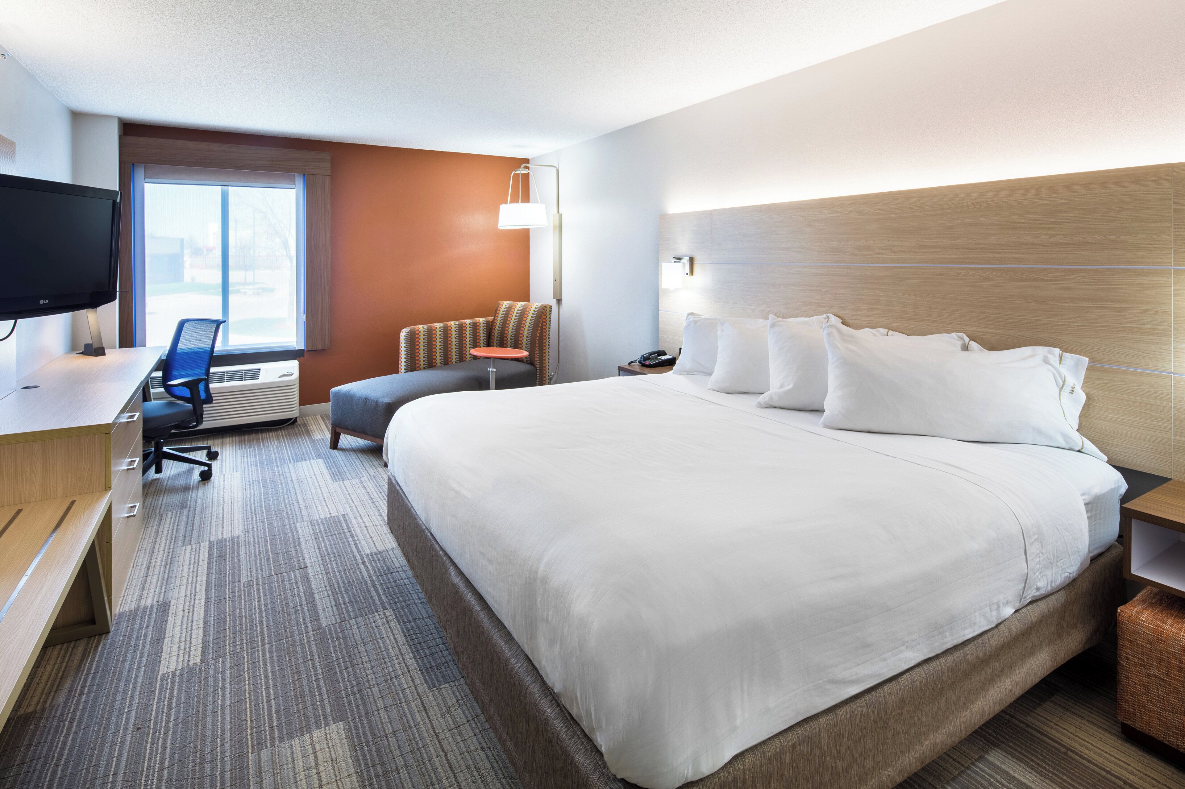 Ein Hotelzimmer mit einem großen Bett, einem Schreibtisch mit Stuhl, einem Fernseher und einem Fenster.