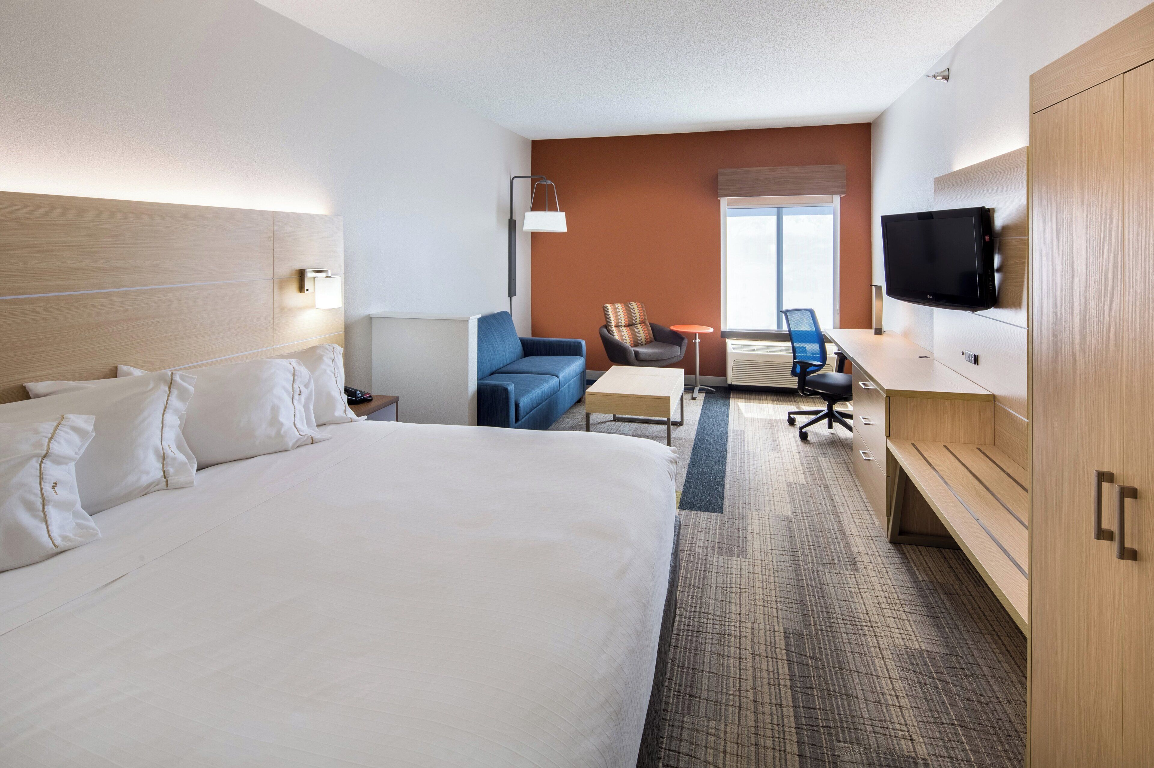 A hotel room with a large bed, a desk, a chair, a TV, and a window.