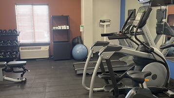 Un gimnasio con cintas de correr, una bicicleta estática y una máquina de remo. Hay mancuernas y una pelota de medicina.