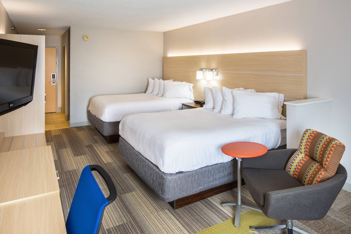 A hotel room with two beds, a TV, a desk, and a chair.