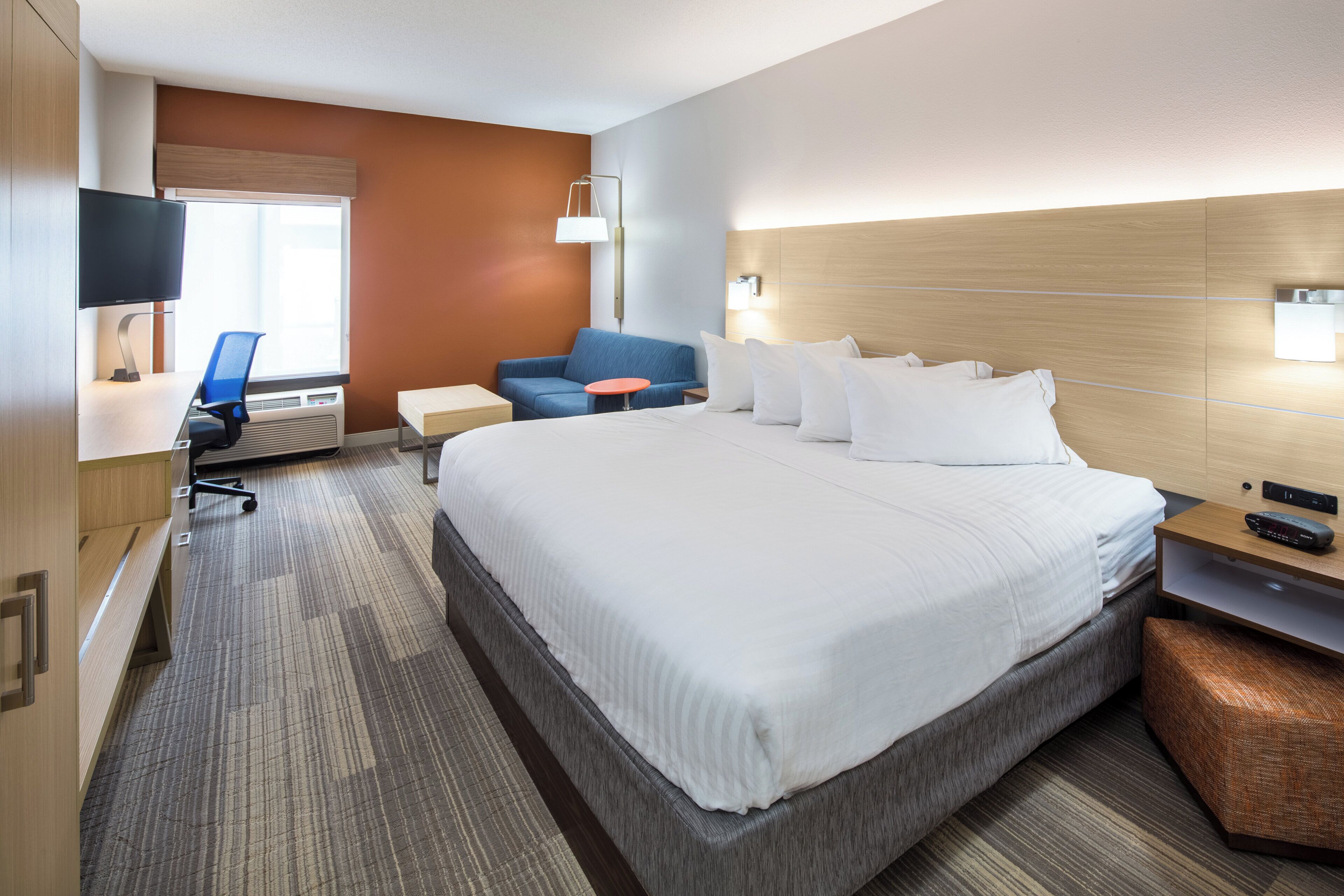 A hotel room with a large bed, a desk with a computer, a chair, a small table, and a television.