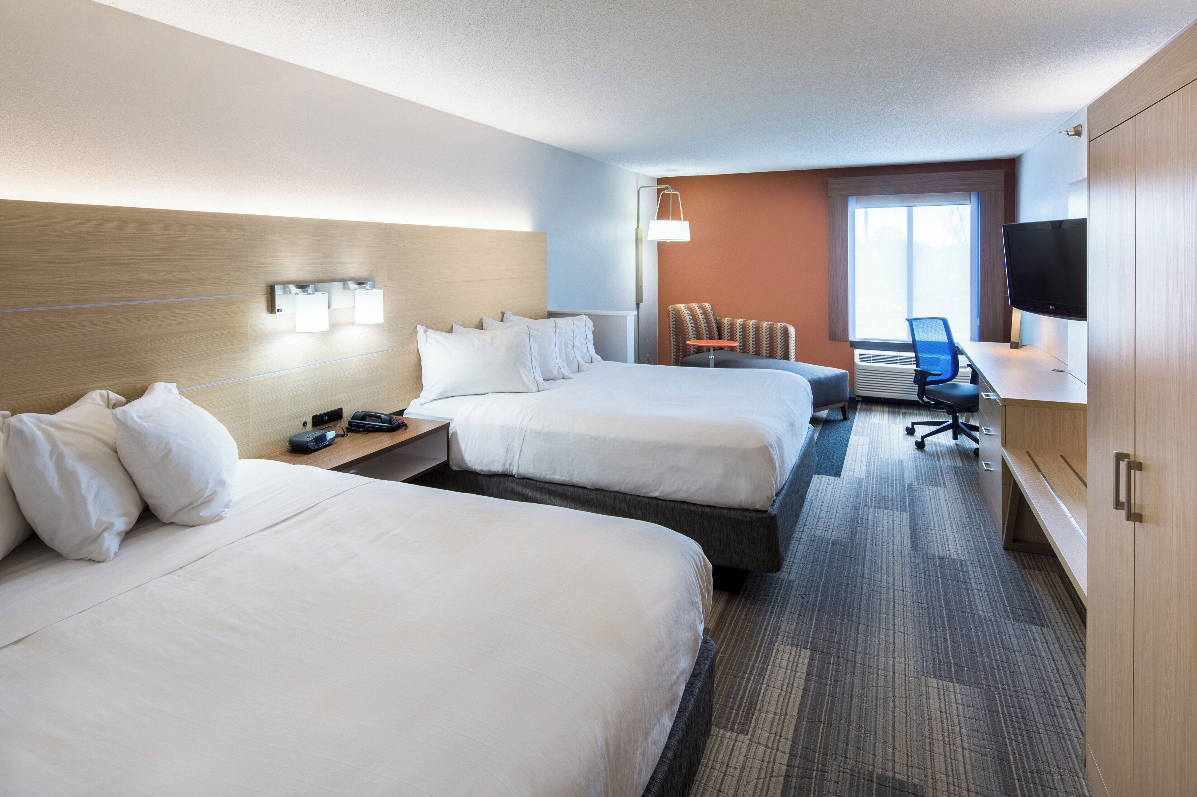 A hotel room with two beds, a desk, a chair, a TV, and a window.