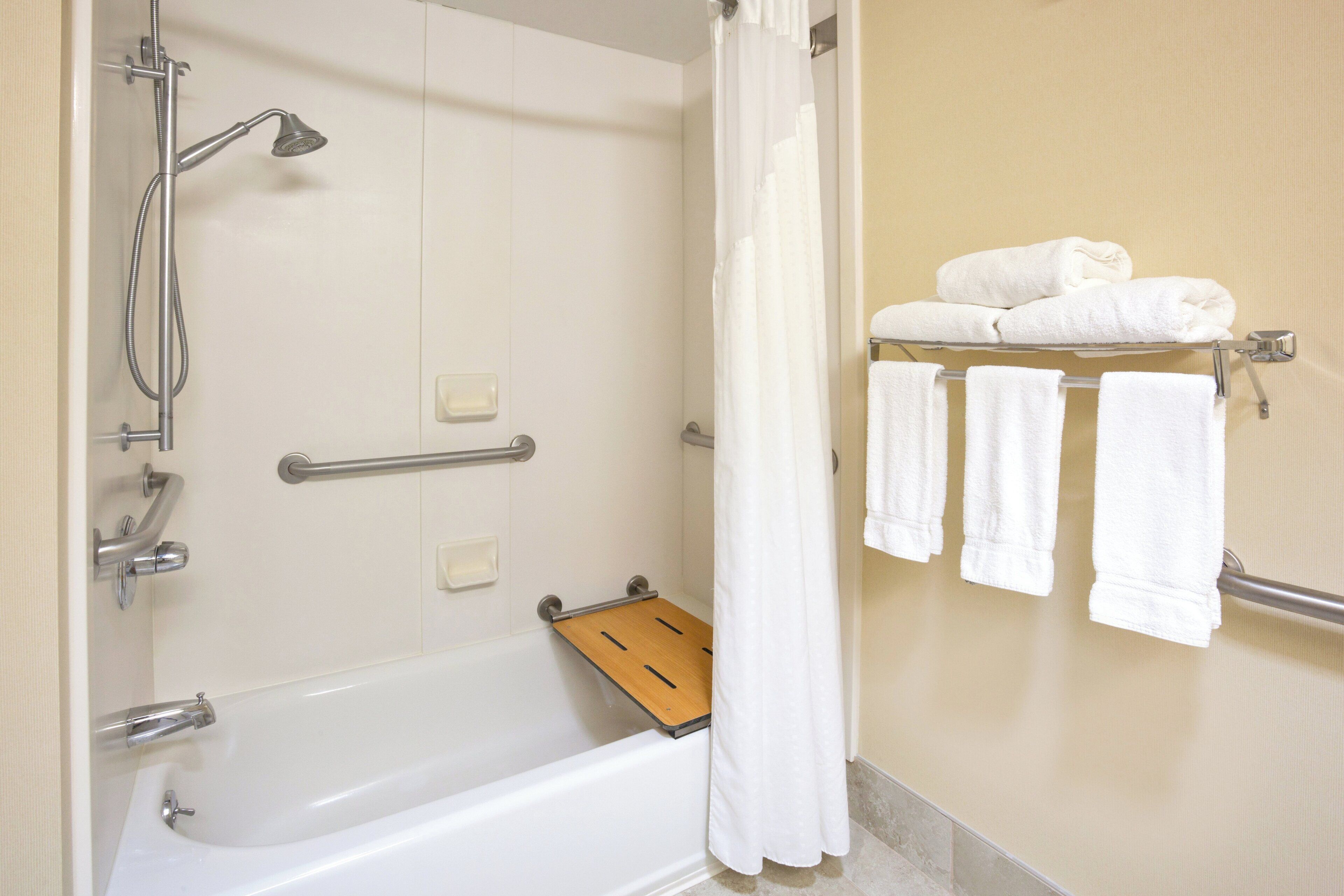 A bathroom with a bathtub, shower, and a towel rack with folded towels.