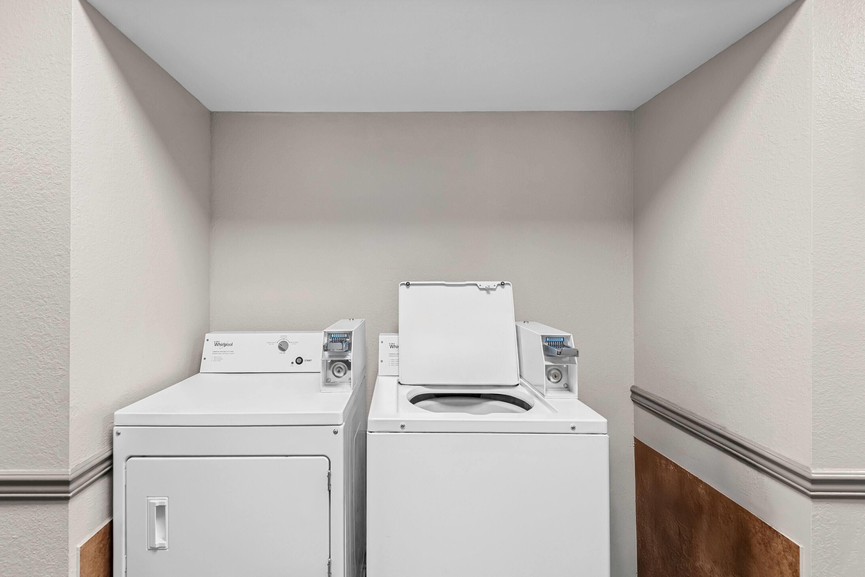 Une buanderie équipée de deux machines à laver et deux sèche-linge superposés, avec des murs blancs et un plintheur en bois.